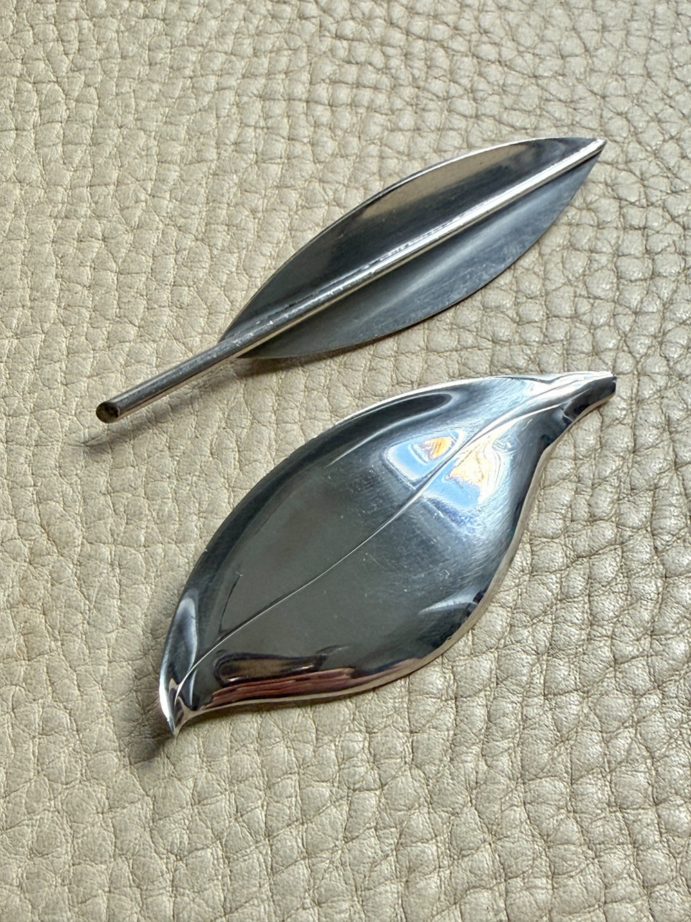 Two silver leaf-shaped brooches on a textured beige surface