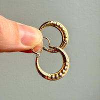 French vintage 18k Gold hoop earrings held between fingers against a neutral background