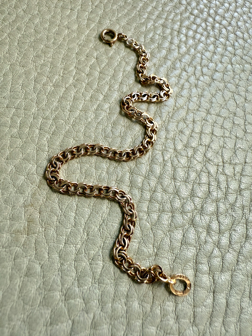 Gold chain bracelet on a textured light green surface