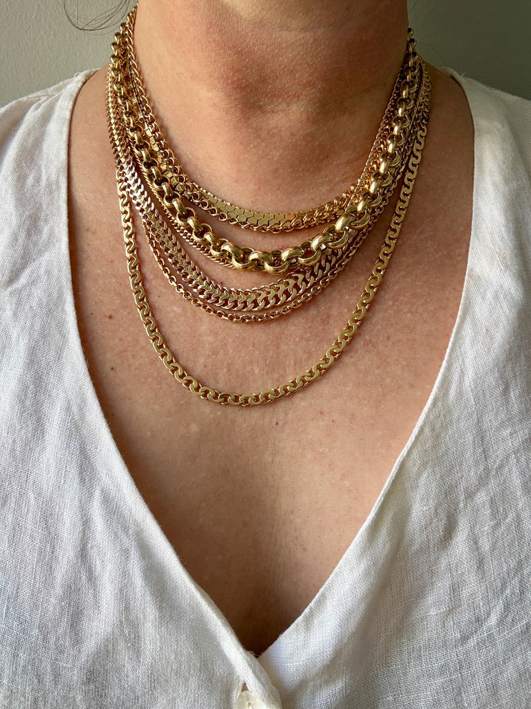 A close-up of a person wearing a layered stack of 18k gold chain necklaces over a white V-neck top.