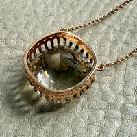 Decorative 18k gold pendant setting on a chain against a textured light background