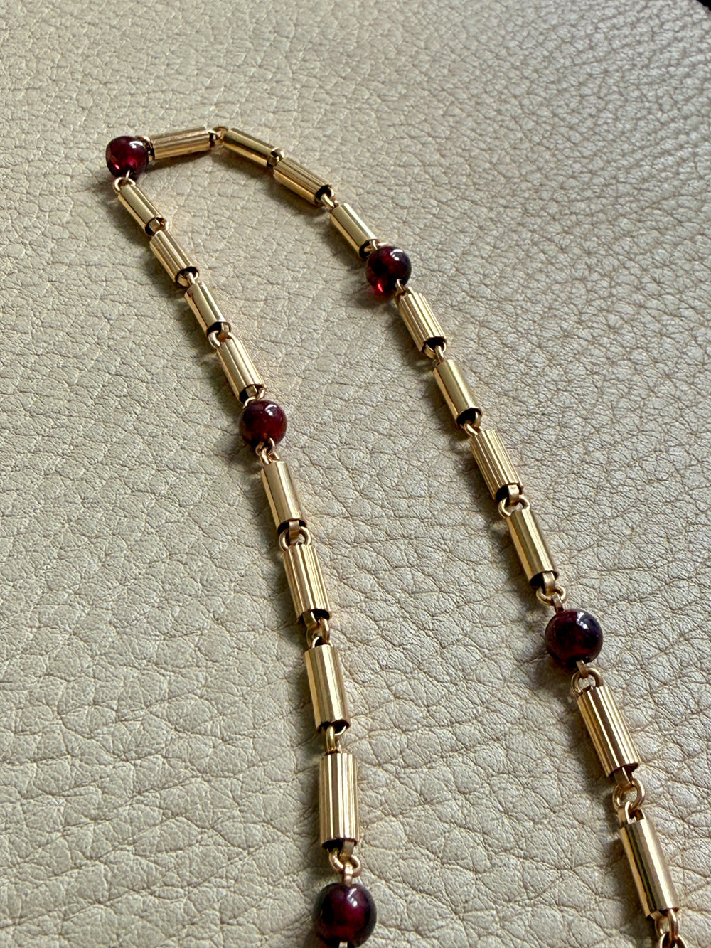 Gold necklace with red beads on a textured beige surface