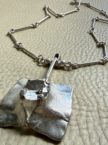 Silver necklace with a unique pendant on a textured surface