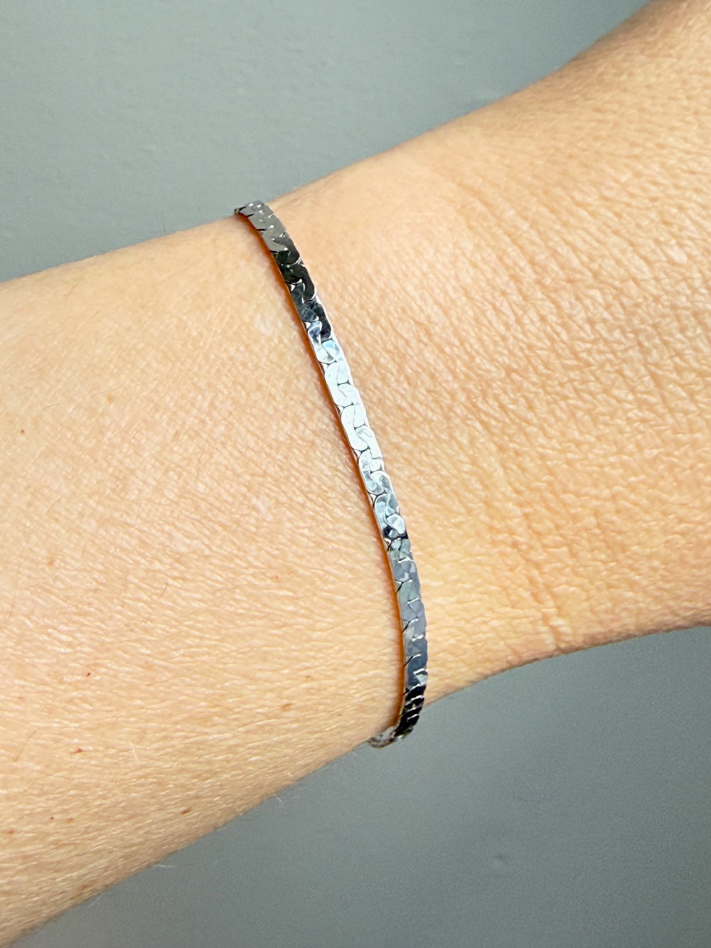 white gold bracelet on a wrist against a gray background