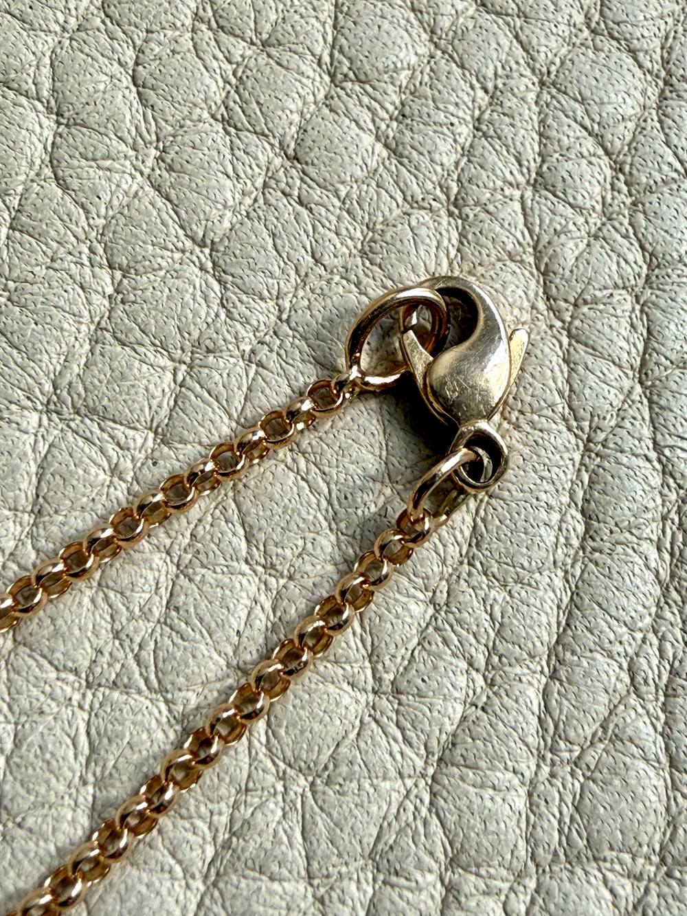 Close-up of a gold chain with a clasp on a textured light gray background