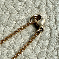 Close-up of a gold chain with a clasp on a textured light gray background