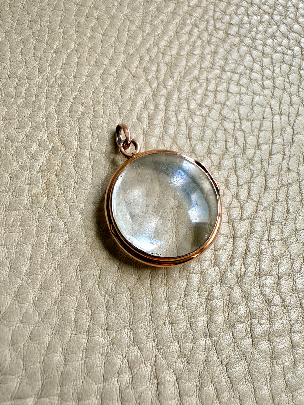 Clear pool of light pendant with rose gold setting on a textured beige surface