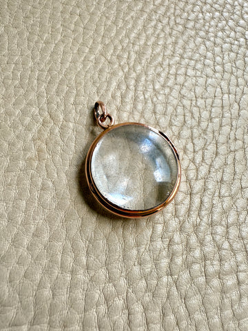 Clear pool of light pendant with rose gold setting on a textured beige surface