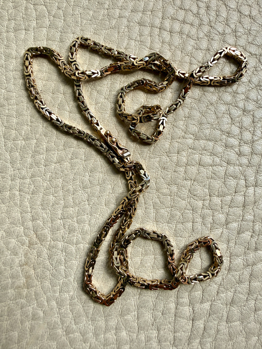 14k gold Gold byzantine chain necklace on a textured beige surface penelopepenelope.com fine jewelry