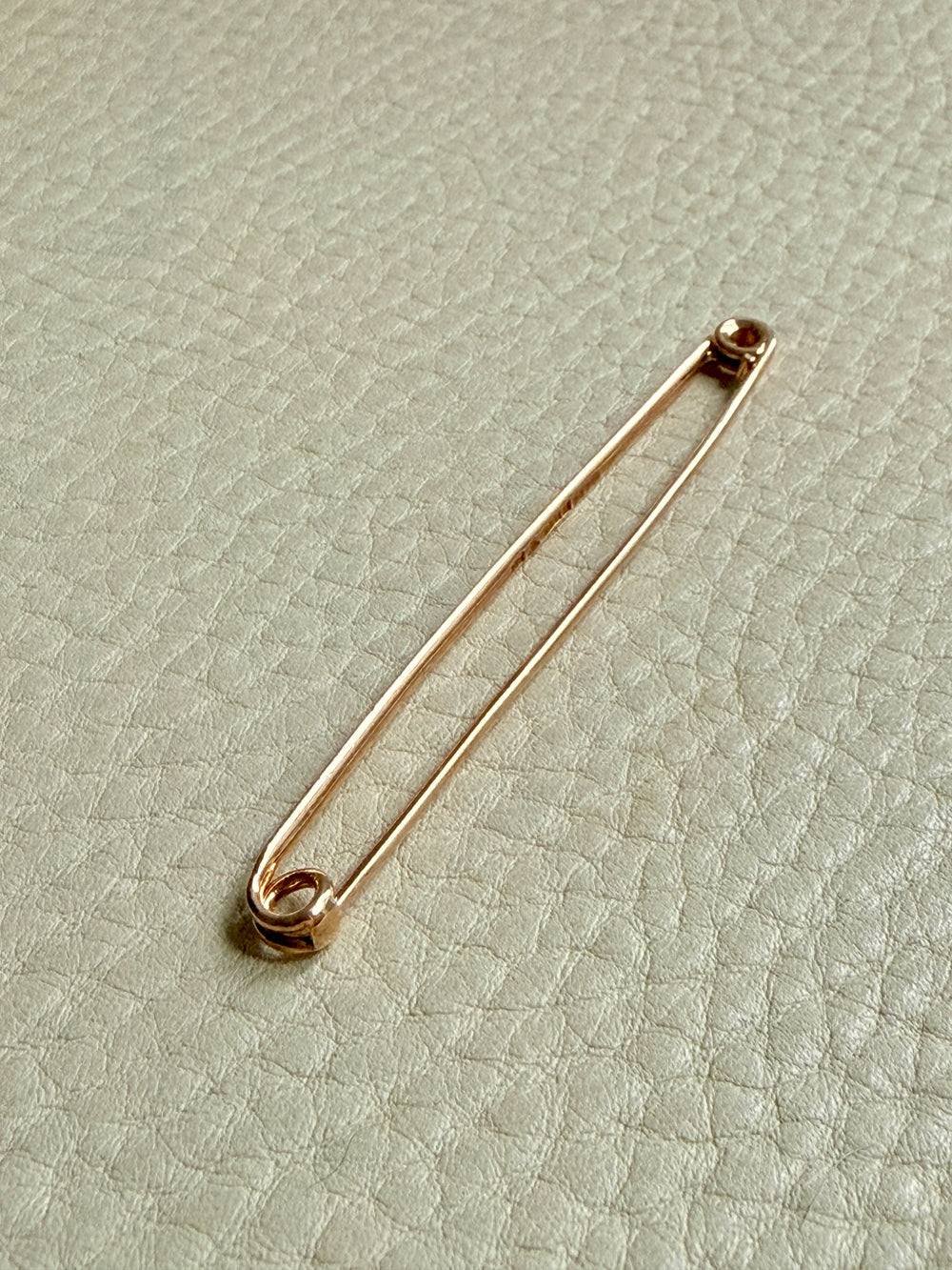 Gold antique safety pin on a textured light green background