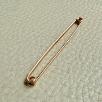 Gold antique safety pin on a textured light green background