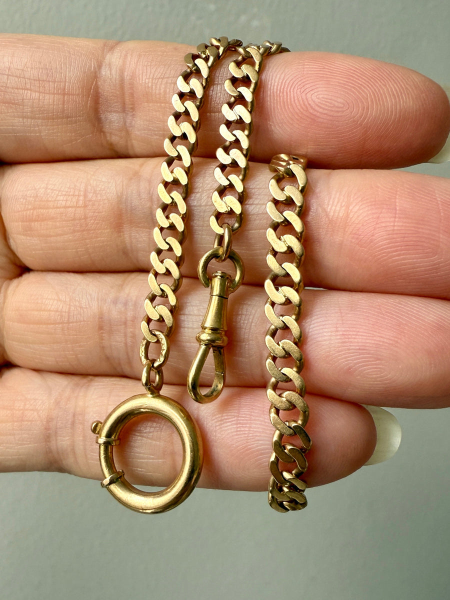 Gold watch chain necklace with bolt ring held between fingers against a neutral background