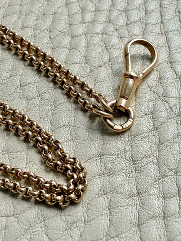 Gold chain necklace with clasp on a textured gray surface