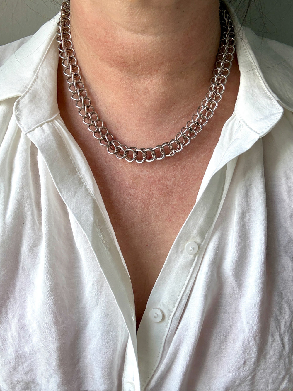 Person wearing a silver chain necklace with a white shirt.