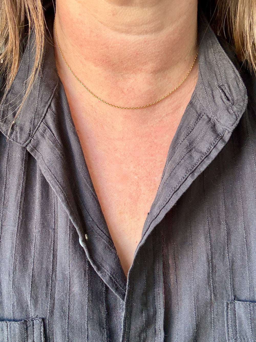 Person wearing a gray shirt with a gold necklace