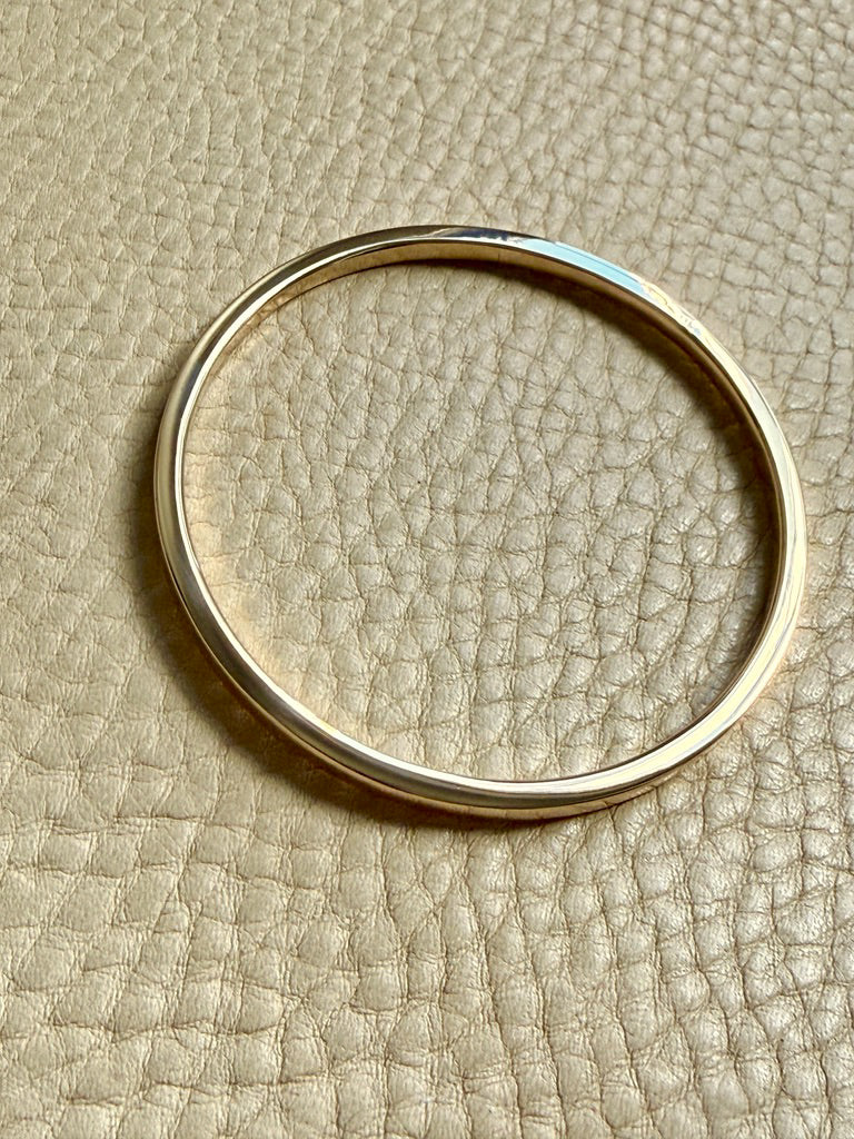 14k Gold solid round bangle on a beige textured surface