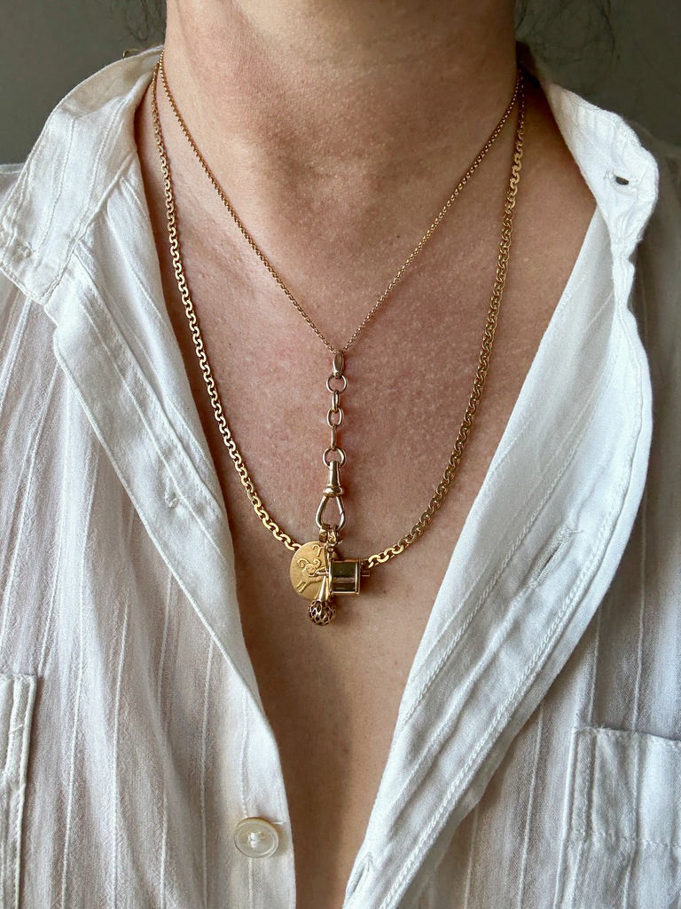Close-up of a person wearing a gold necklace with a pendant, against a neutral background. Penelope Penelope Vintage Jewelry