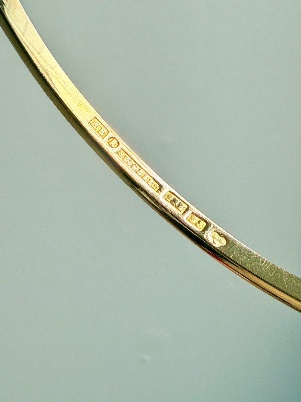 Close-up of a gold bracelet with hallmark stamps details on a light blue background