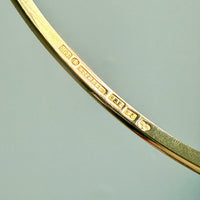 Close-up of a gold bracelet with hallmark stamps details on a light blue background