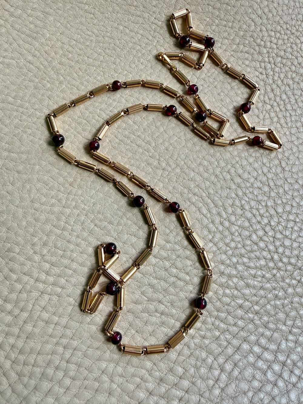 18k Gold necklace with red beads on a textured beige surface