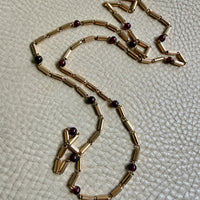 18k Gold necklace with red beads on a textured beige surface