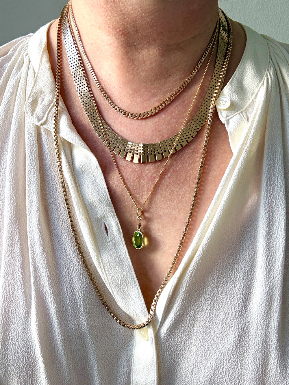 Close-up of a person wearing multiple gold necklaces with a green pendant on a white shirt.