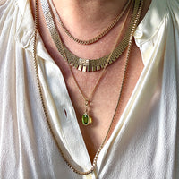 Close-up of a person wearing multiple gold necklaces with a green pendant on a white shirt.