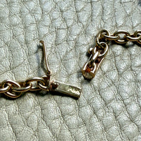 14k gold oval link Gold necklace clasp detail on a textured light gray surface