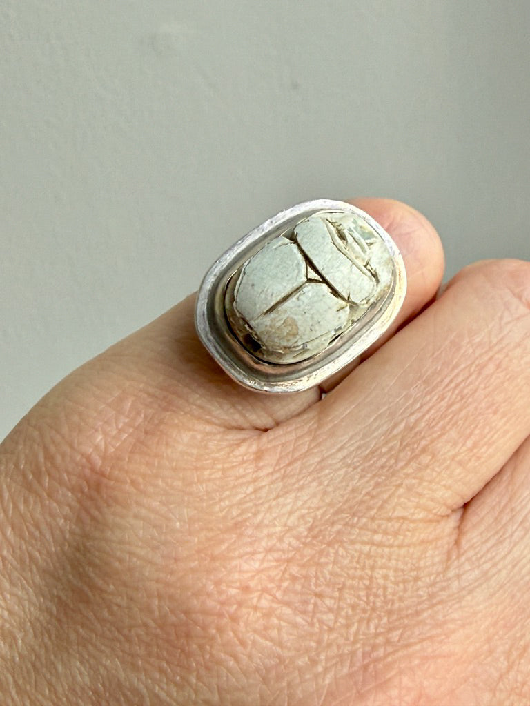 A close-up of a hand wearing a chunky silver ring with a textured, cracked stone scarab beelte inlay.