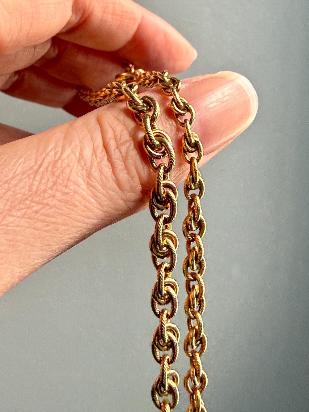 Gold chain held between fingers against a gray background