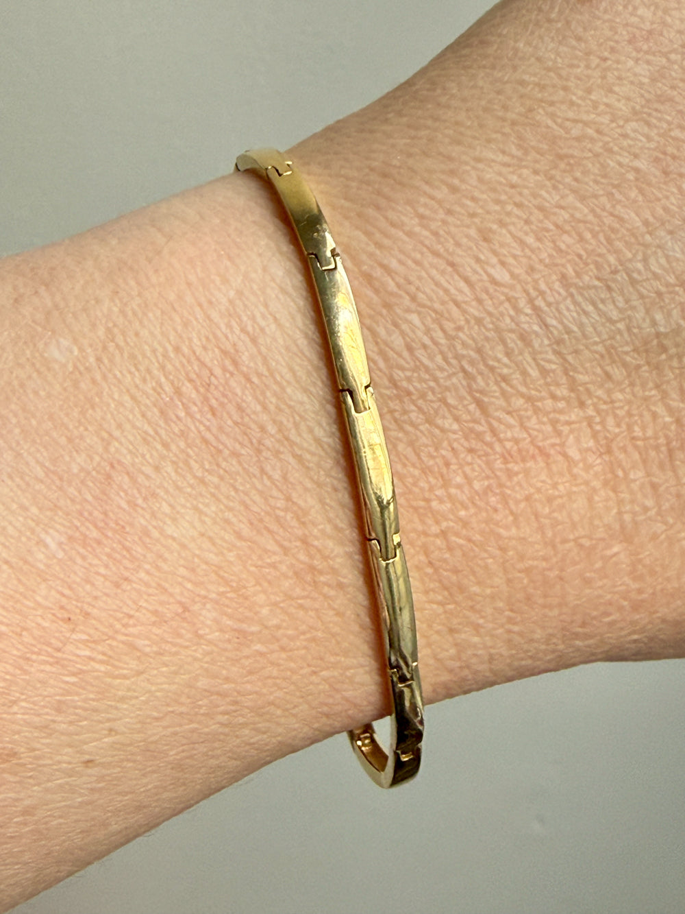 Gold bracelet on a wrist against a neutral background
