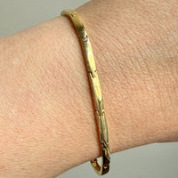 Gold bracelet on a wrist against a neutral background