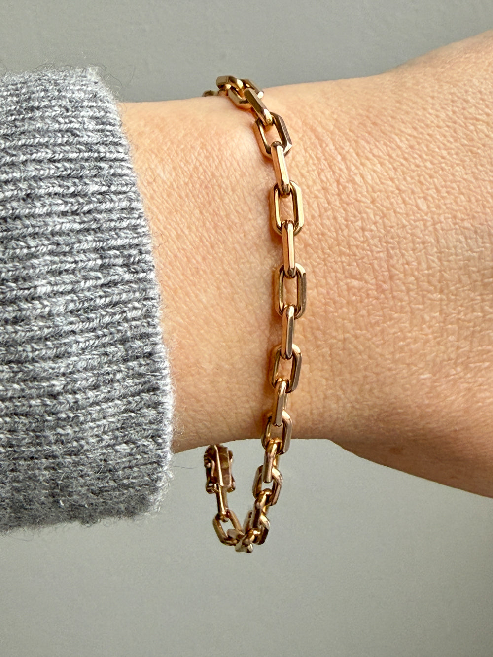 18k Gold biker link chain bracelet on a wrist with a neutral background