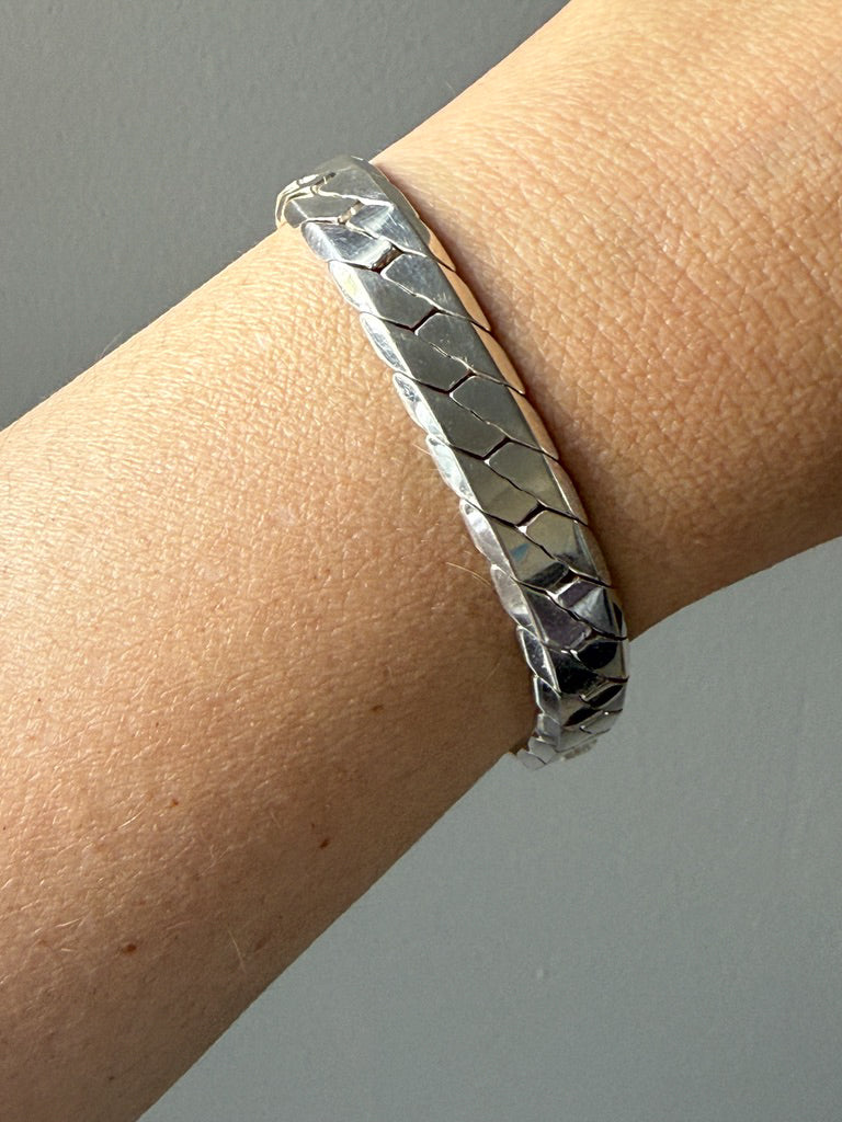 Silver bracelet on a wrist against a neutral background
