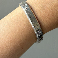 Silver bracelet on a wrist against a neutral background