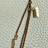 Gold necklace with a tag on a textured light green background