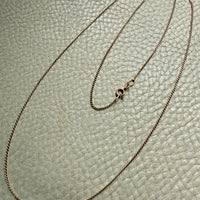 Gold chain necklace on a textured light green surface