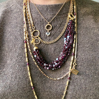 Person wearing multiple necklaces with a focus on gold and maroon chains.