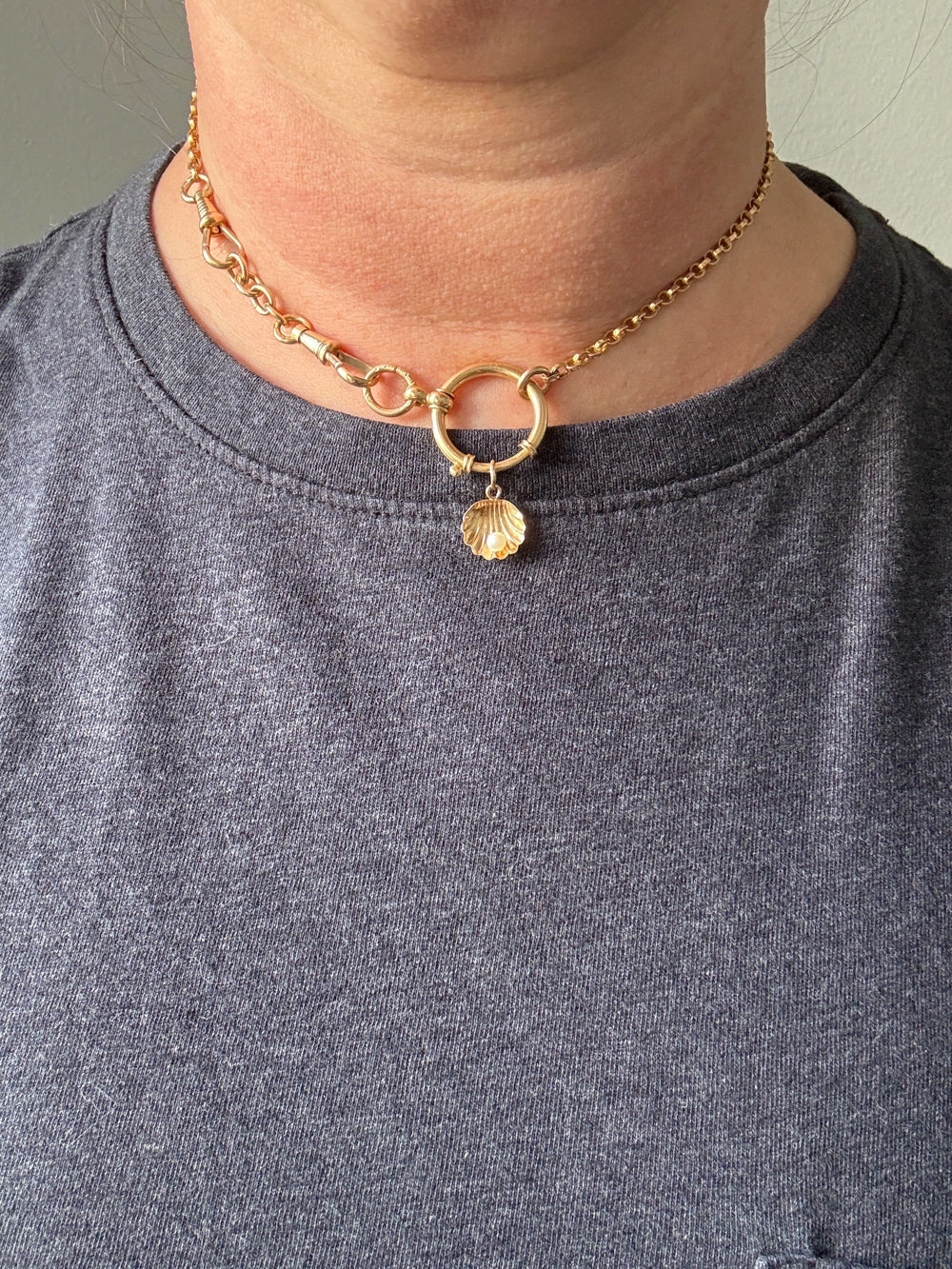 Gold necklace with a shell charm worn by a person in a gray shirt.