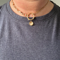 Gold necklace with a shell charm worn by a person in a gray shirt.