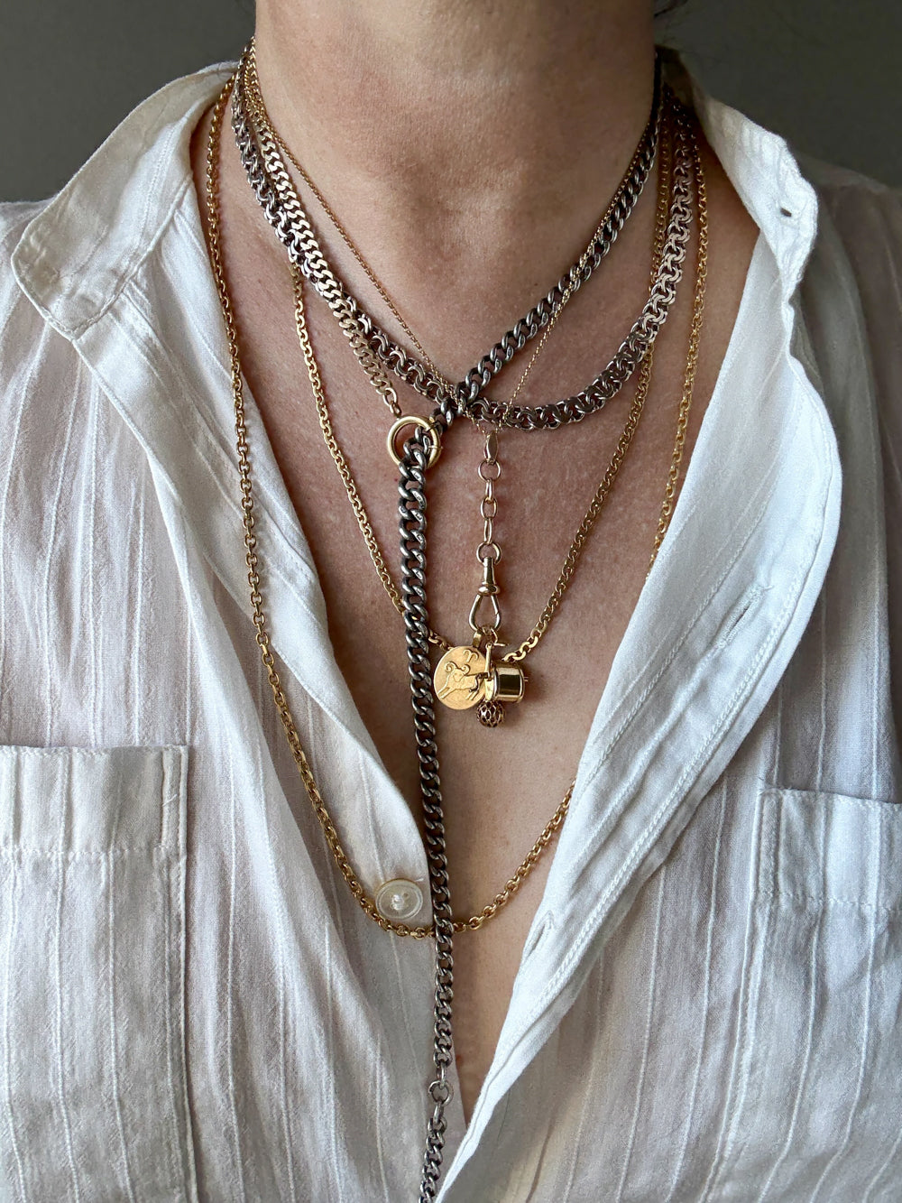 Close-up of layered necklaces on a person wearing a white shirt.