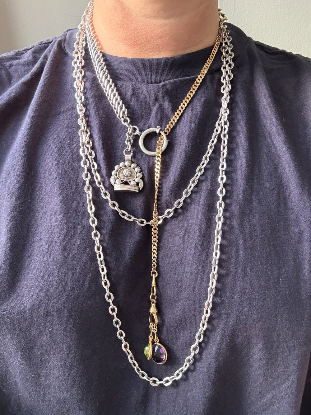 Necklace with multiple chains and pendants on a person wearing a dark blue shirt.