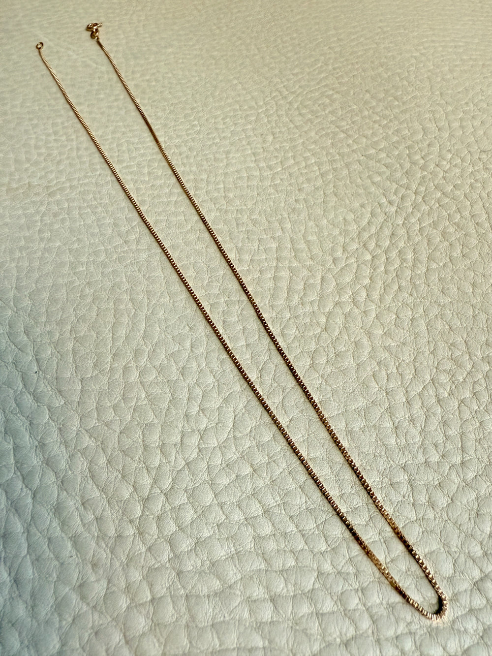 Gold chain necklace on a textured light gra surface