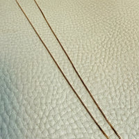 Gold chain necklace on a textured light gra surface