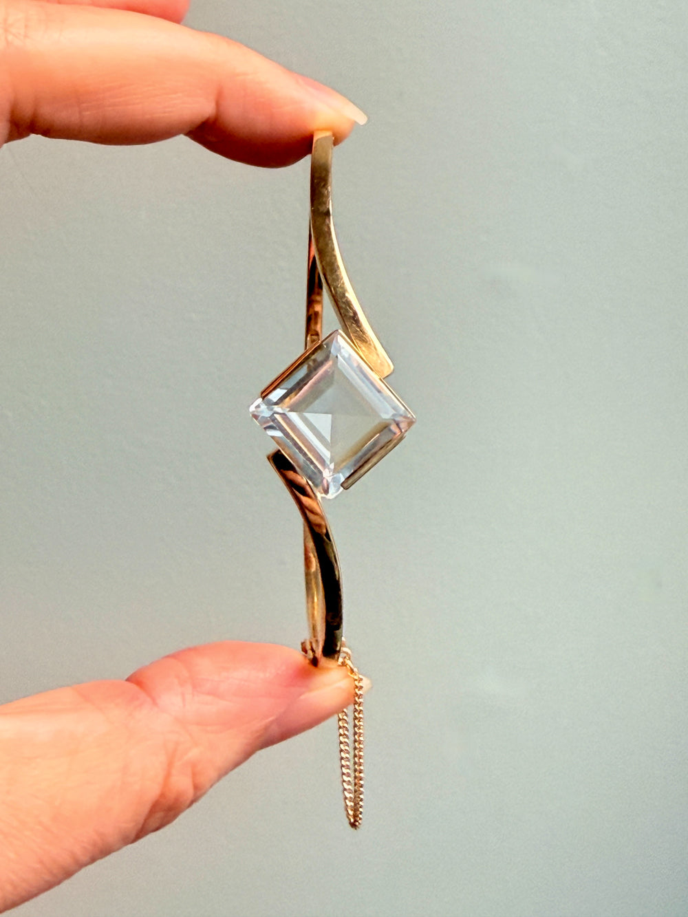 Gold pendant with a clear crystal held by a hand against a light gray background