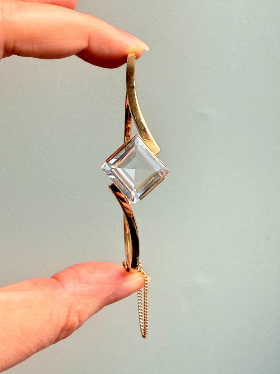 Gold pendant with a clear crystal held by a hand against a light gray background