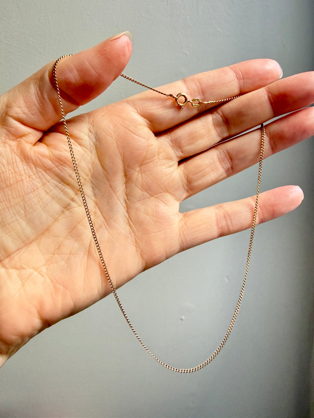 Gold chain held in a hand against a gray background