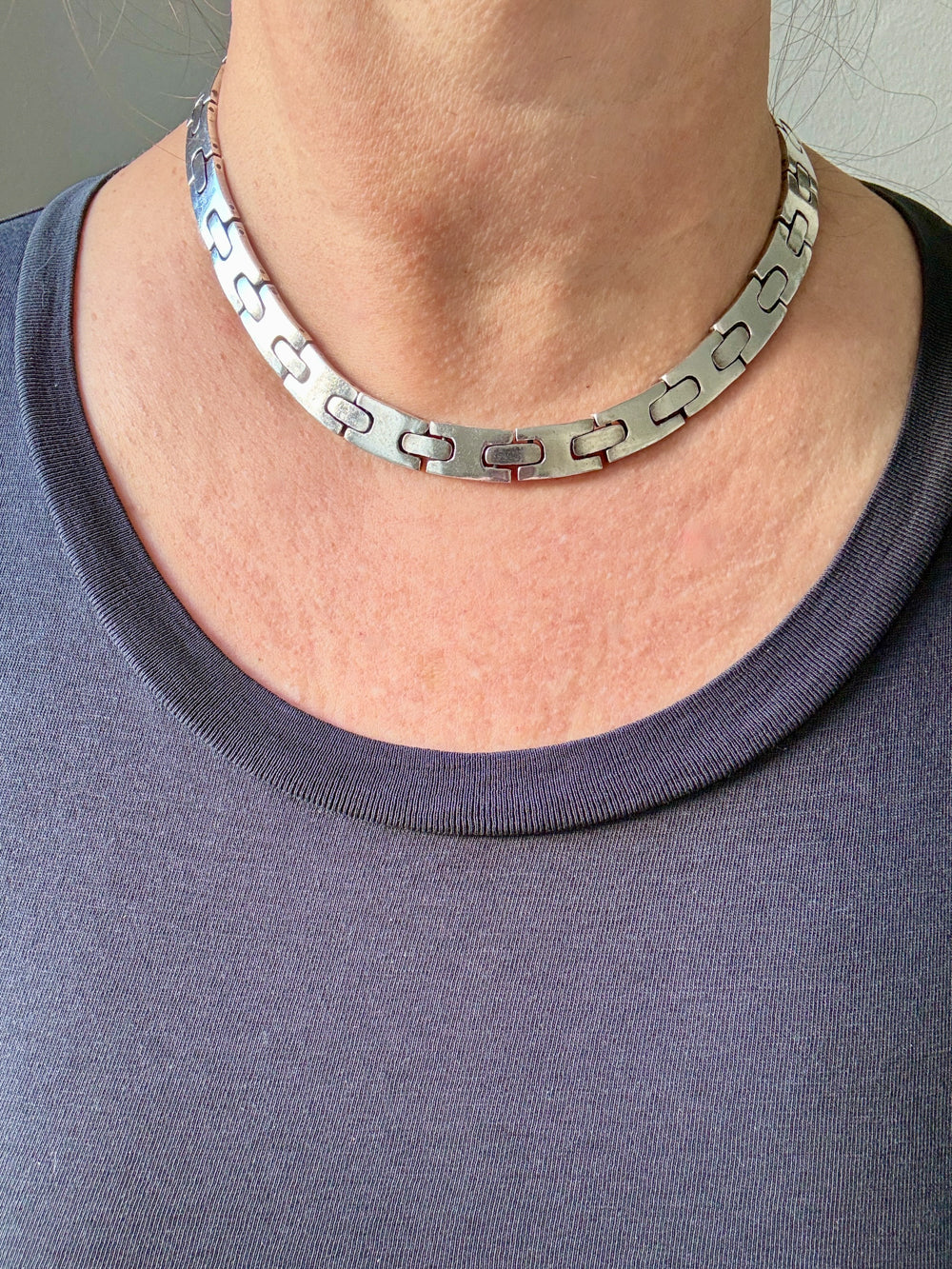 Person wearing a silver chain necklace with a plain background