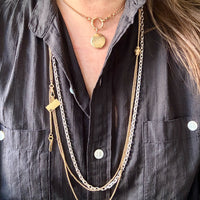 Person wearing multiple gold necklaces with a dark shirt
