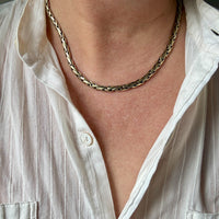 A close-up of a person wearing a braided gold chain necklace over a white button-up shirt.